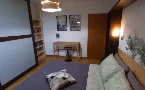 Camera matrimoniale con scrivania in legno, sedia, libreria e stampe alle pareti
