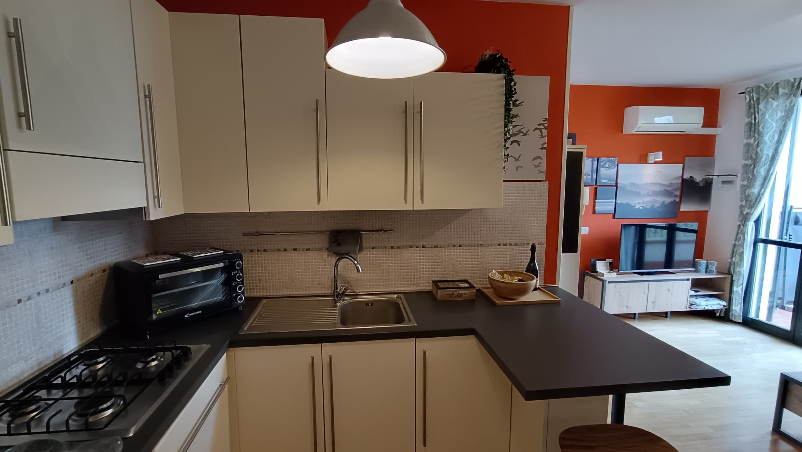 Angolo cottura con piano a gas, forno, lavello, pensili chiari e penisola in laminato scuro